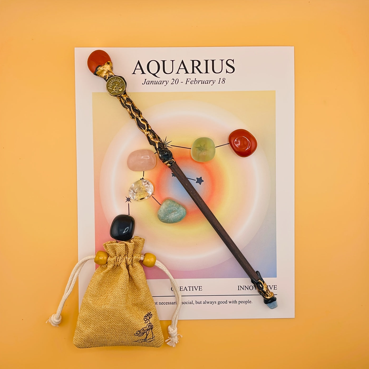 Decorative wand with beads and a small bag on an Aquarius zodiac card against an orange background