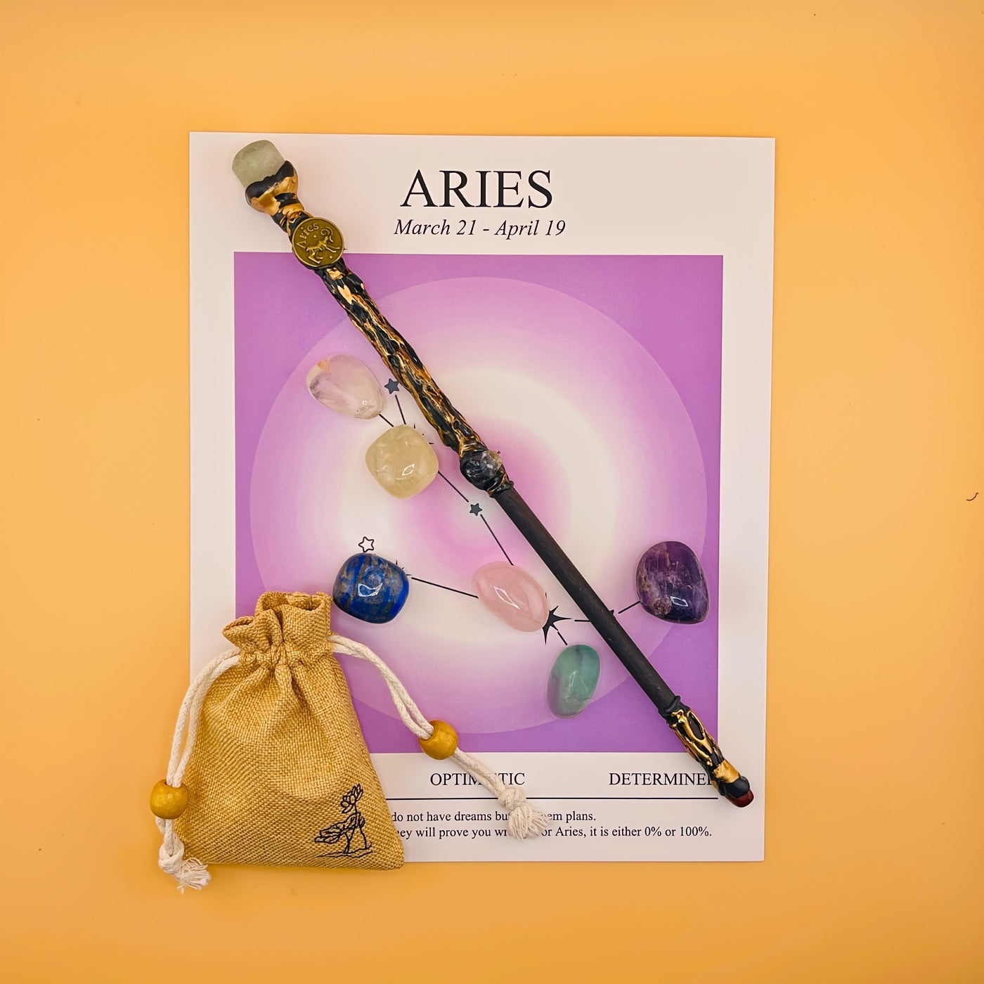 Decorative wand with crystals on an Aries zodiac card against a yellow background