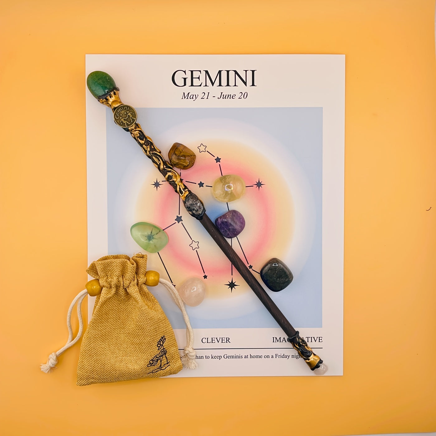 Decorative wand with stones on a Gemini zodiac card against an orange background