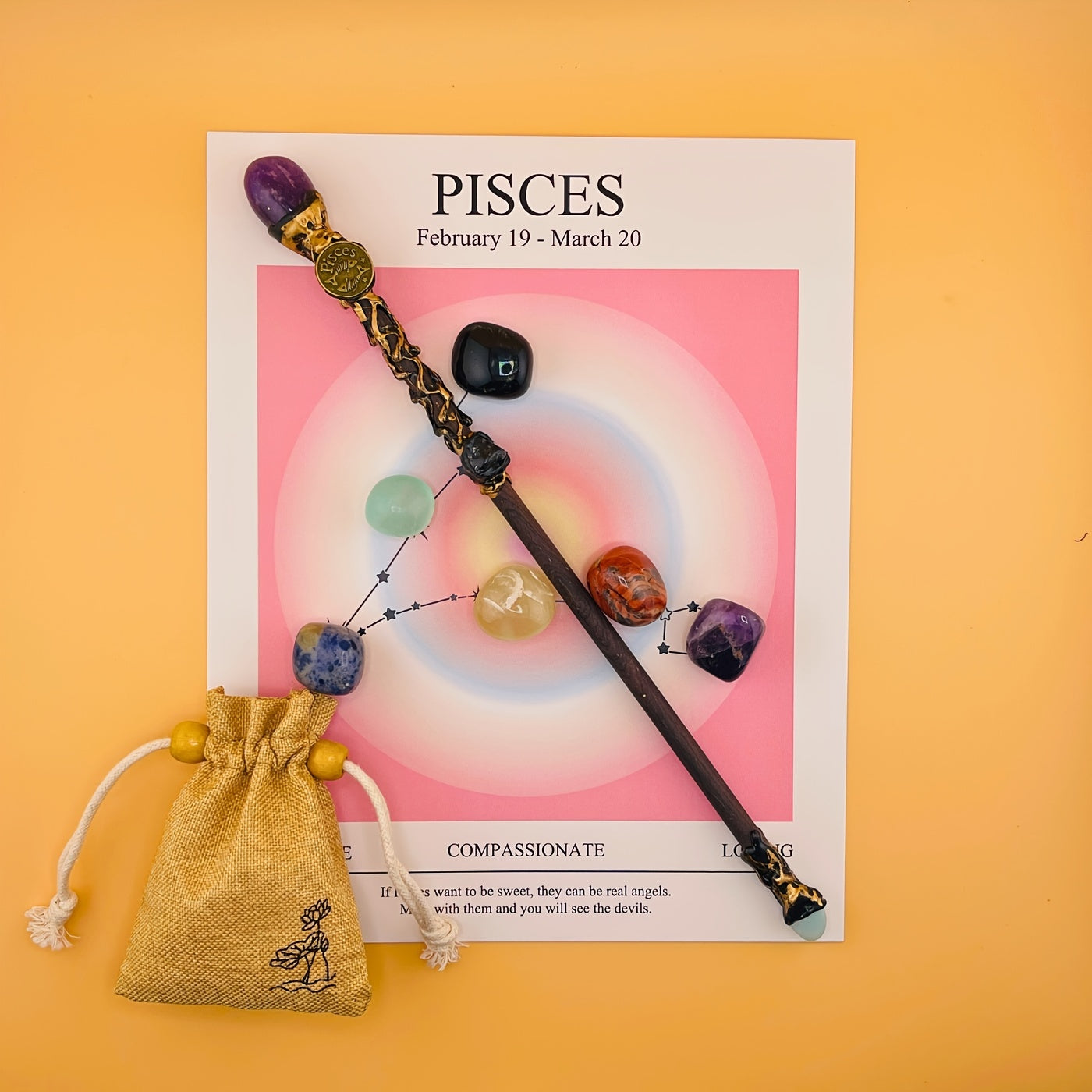 Decorative wand with colorful stones on a Pisces zodiac card against an orange background